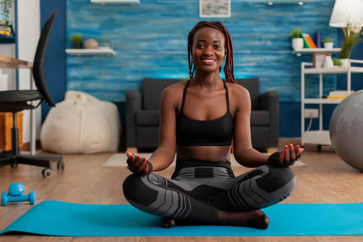 spotcovery-fit-black-woman-practicing-yoga-sitting-with-legs-crossed-sportive-top-leggins-lotus-pose-practicing-calm-mind-harmony-no-stress-life-home-living-room-mindfulness-meditation