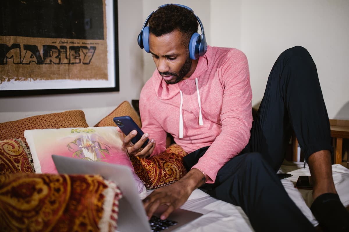 spotcovery-man-in-a-man-with-blue-headphones-holding-his-phone-near-a-laptop-10-money-making-skills-you-can-learn-online-as-a-black-professional