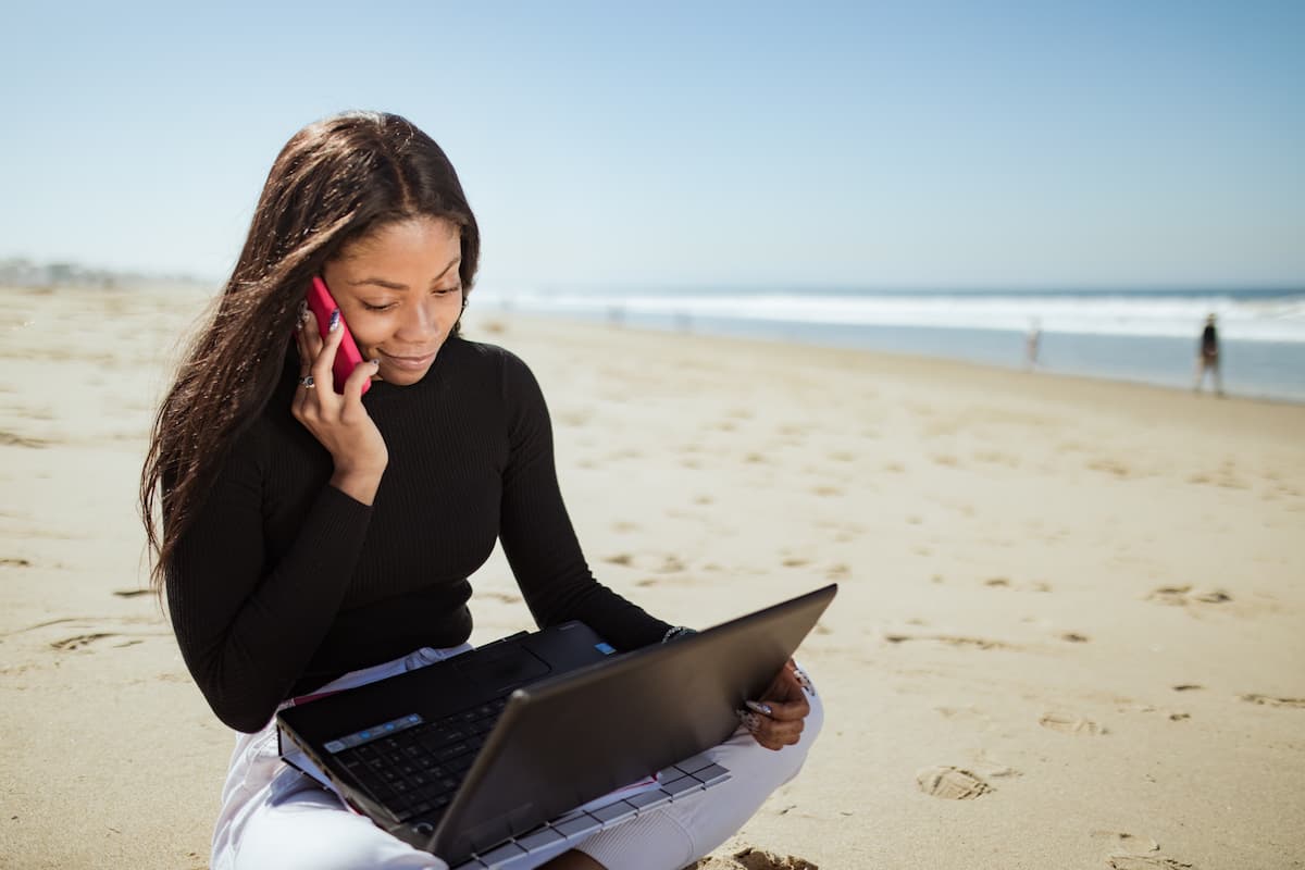 spotcovery-a-woman-in-black-long-sleeve-shirt-using-laptop-computer-on-beach-6-remote-jobs-that-offer-travel-opportunities-for-black Professionals