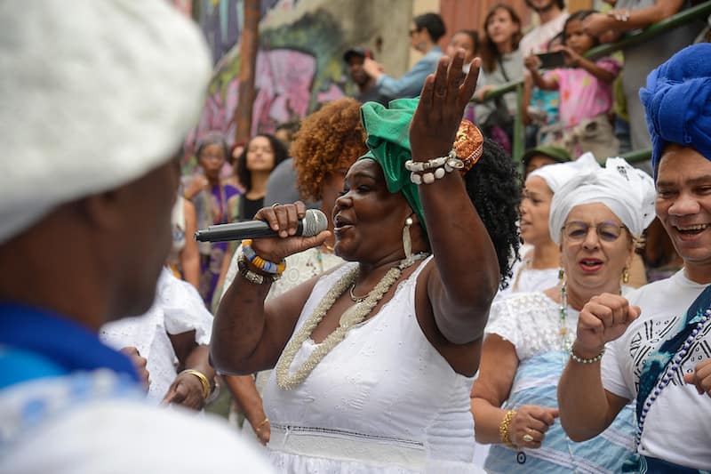 spotcovery-a-woman-wearing-white-in-a-crowd-singing-during-the-festa-literária-das-periferias