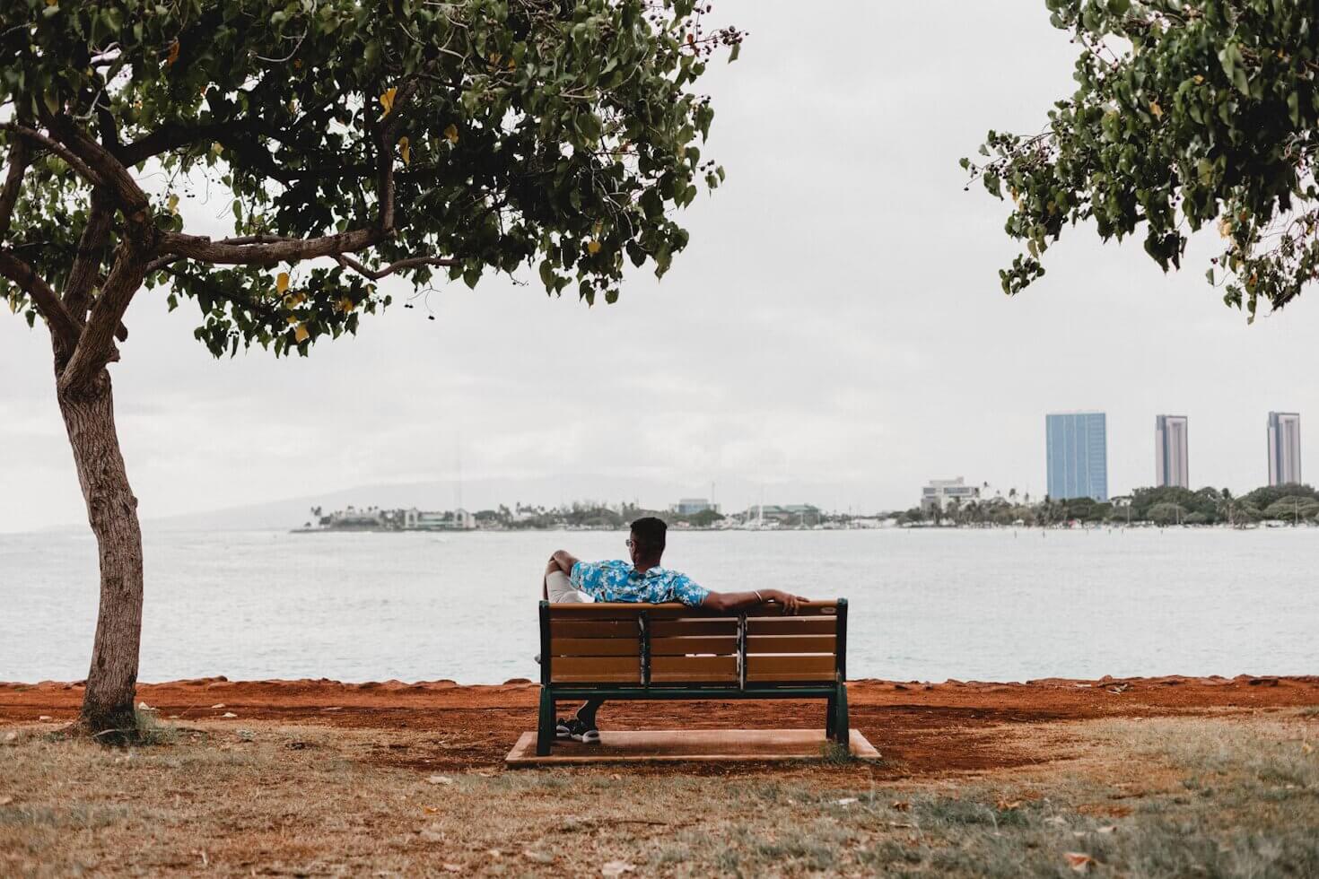 spotcovery-a-man-sitting-on-bench-facing-calm-sea.world-introvert-day